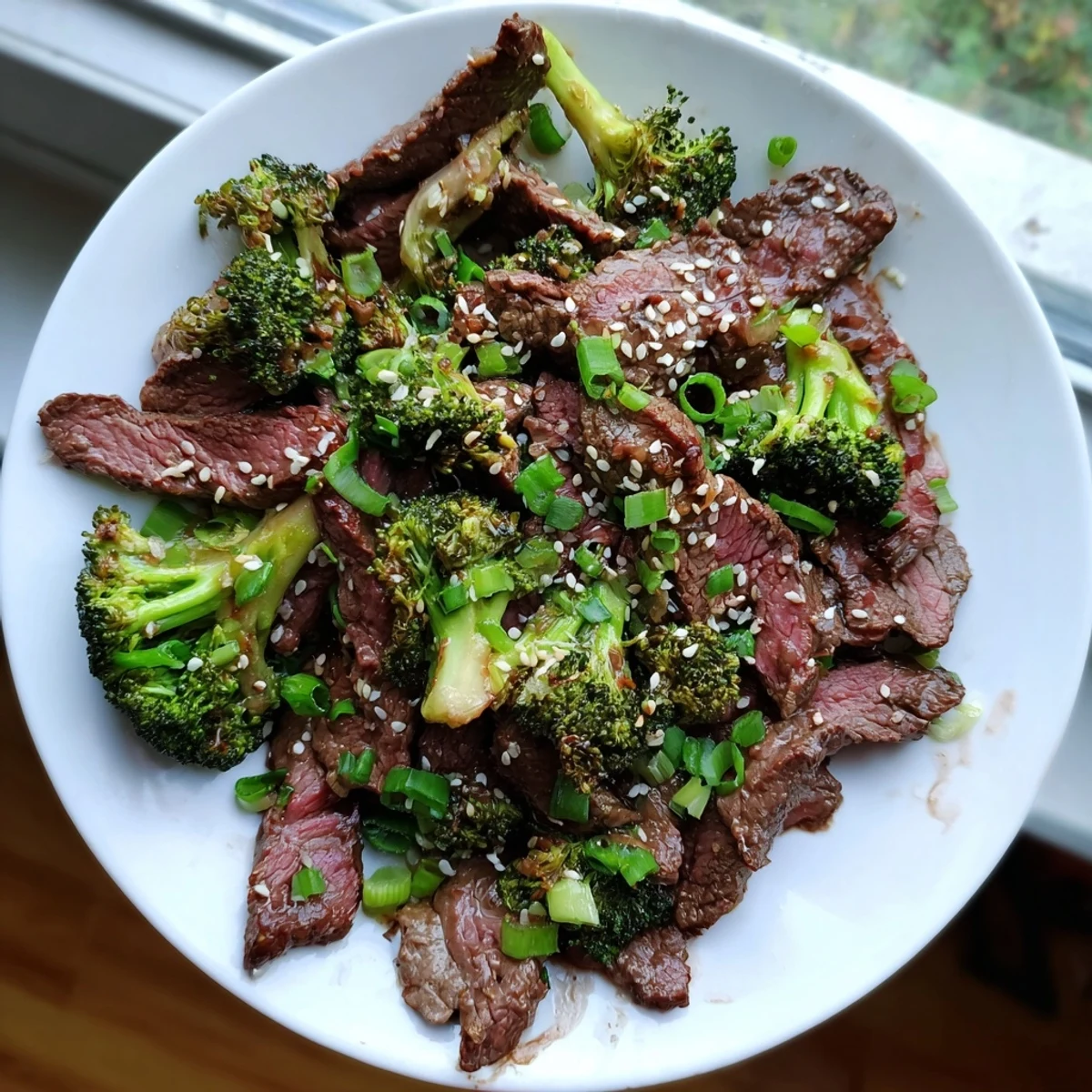 Hearty Keto Friendly Beef and Broccoli Stir Fry with Ginger garnished with fresh green onions and sesame seeds, ready to enjoy with cauliflower rice.