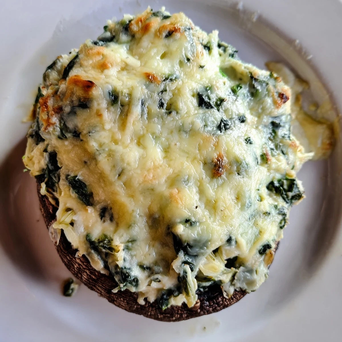 Golden-brown Cheesy Spinach and Artichoke Stuffed Portobello Mushrooms with melted cheese bubbling over the edges.