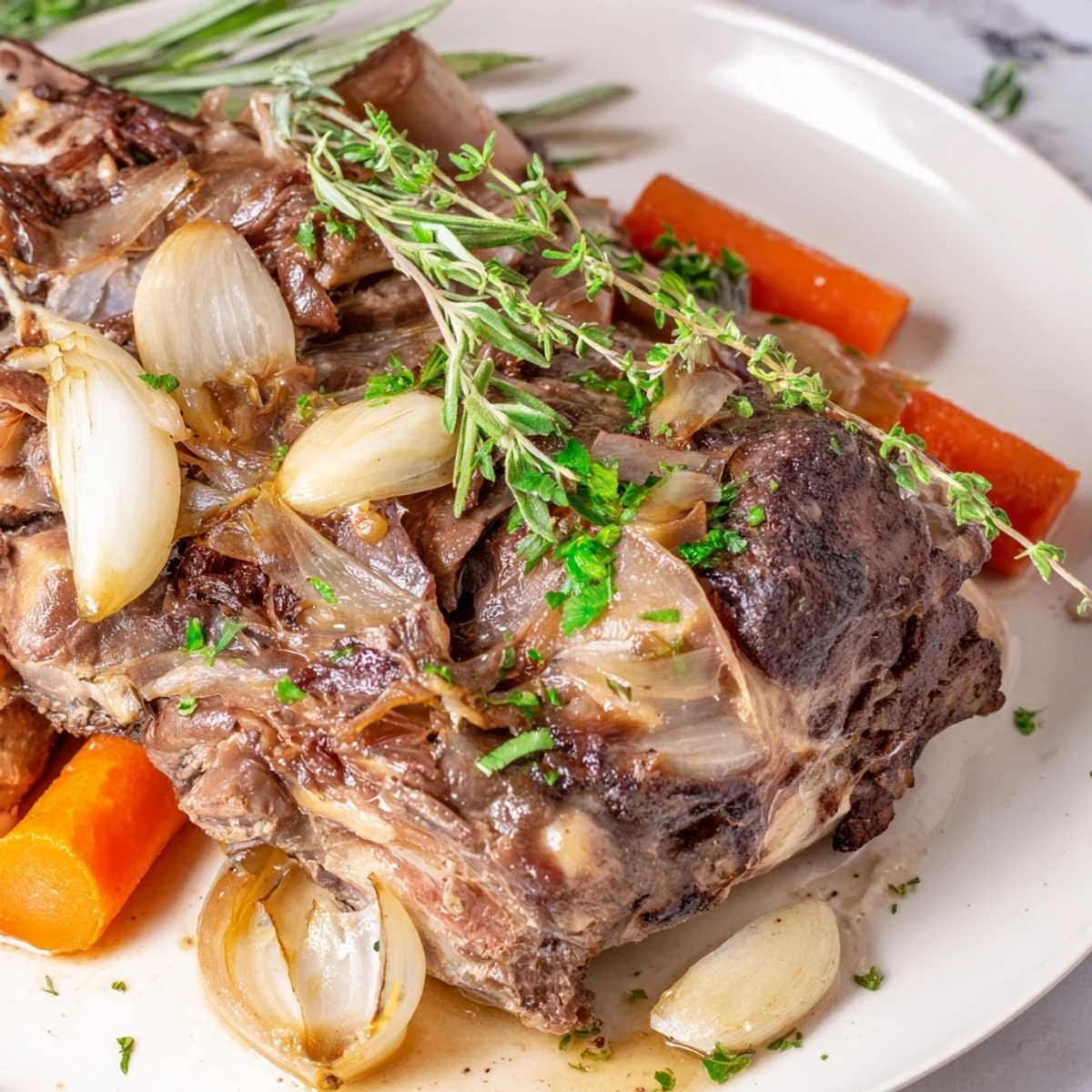 Fresh rosemary sprigs and golden garlic cloves stud this Slow Cooked Lamb Shoulder with Garlic and Herbs for aromatic flavor.