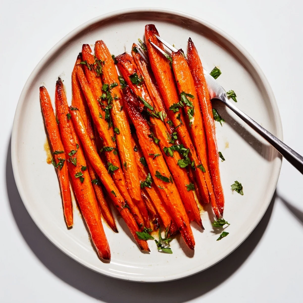 Bright orange roasted carrots glistening with a sweet maple glaze, served warm on a white platter garnished with fresh parsley.  