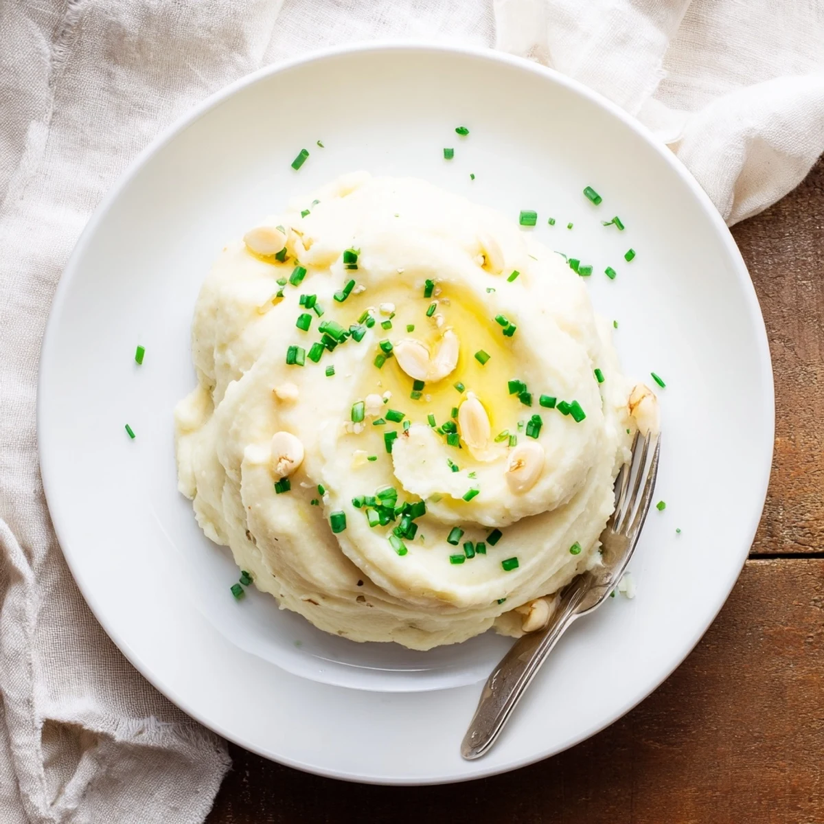 A close-up of creamy Roasted Garlic Mashed Cauliflower in a rustic bowl, garnished with fresh chives and a pat of butter.