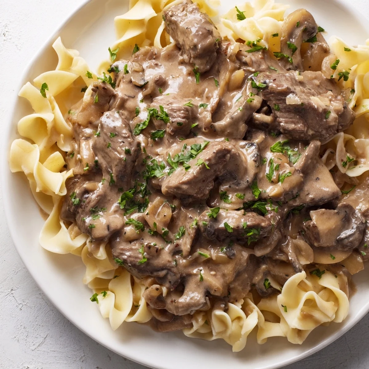 Hearty Beef Stroganoff with mushroom gravy served over noodles, garnished with fresh parsley on a rustic dinner plate.