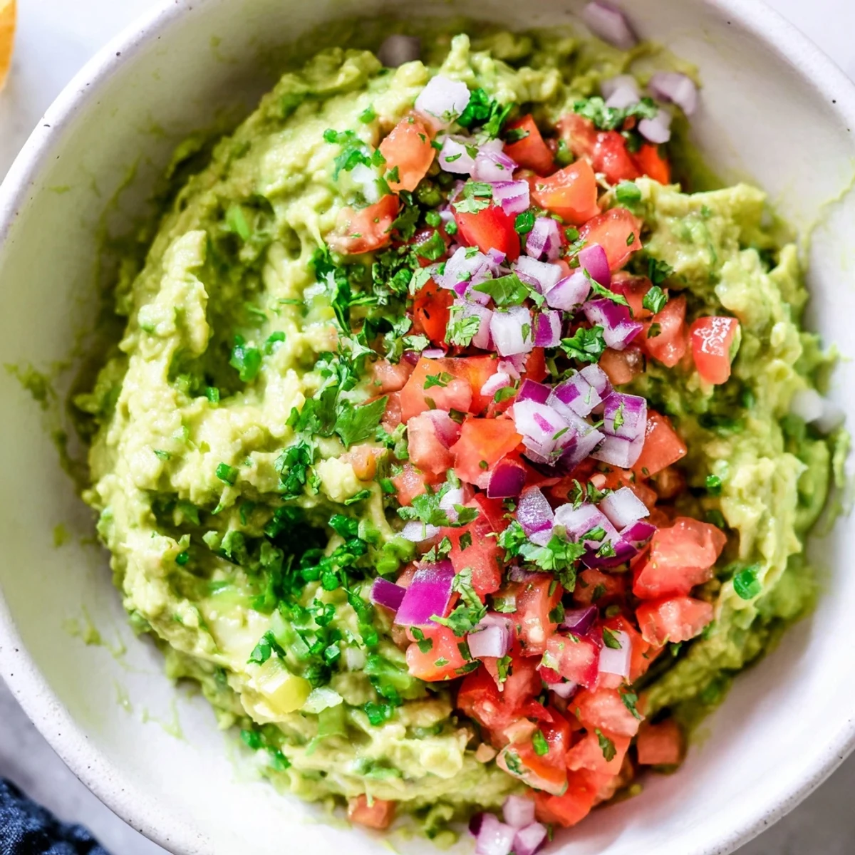 A festive bowl of Super Bowl Guacamole topped with fresh salsa, ready for game day snacking with chips.