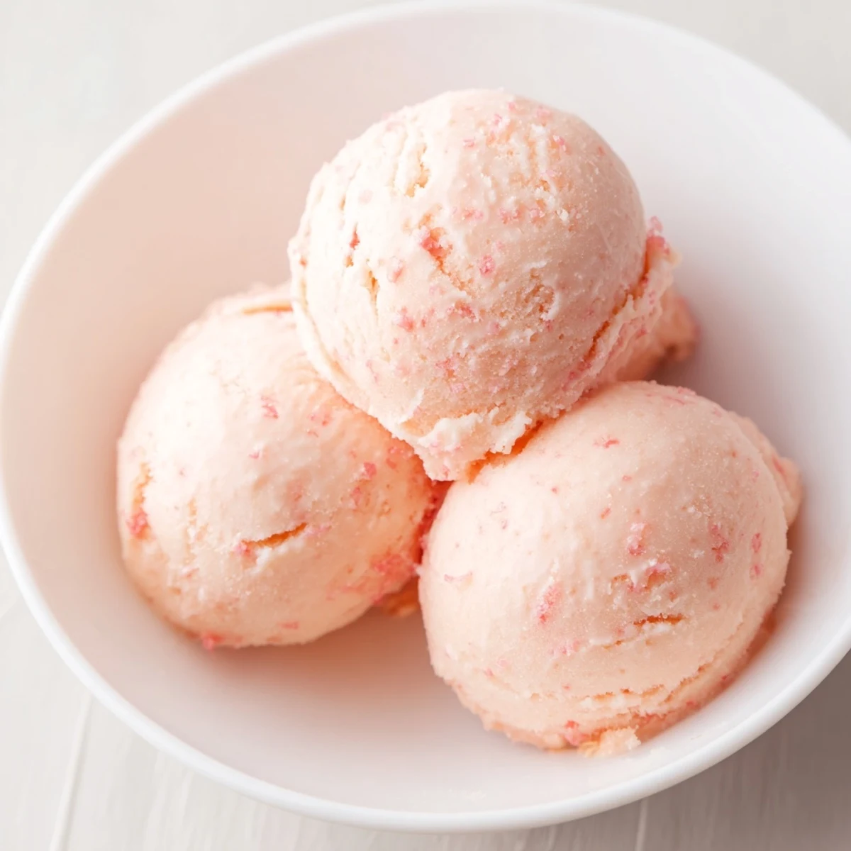 Fresh scoops of Pink Grapefruit Sorbet in a glass bowl, garnished with mint and zest.
