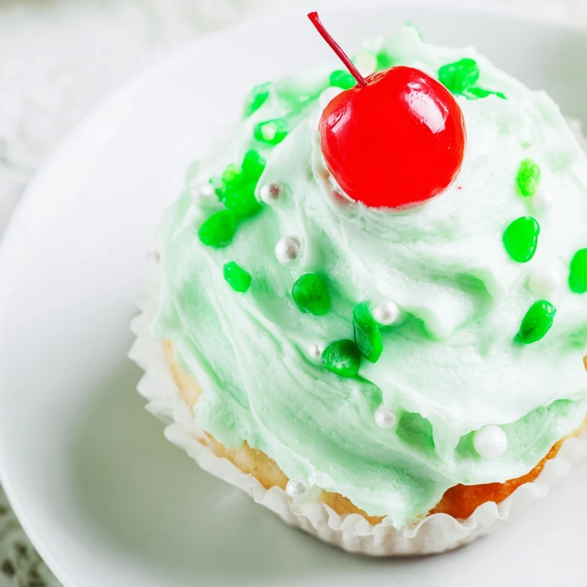 A platter of freshly baked Shamrock Shake Cupcakes with creamy mint frosting and maraschino cherries.
