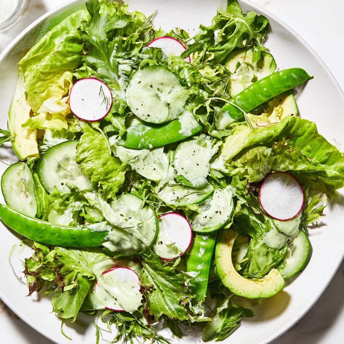 A close-up of Green Salad with Green Goddess Dressing, creamy green sauce drizzled over crisp romaine and butter lettuce.