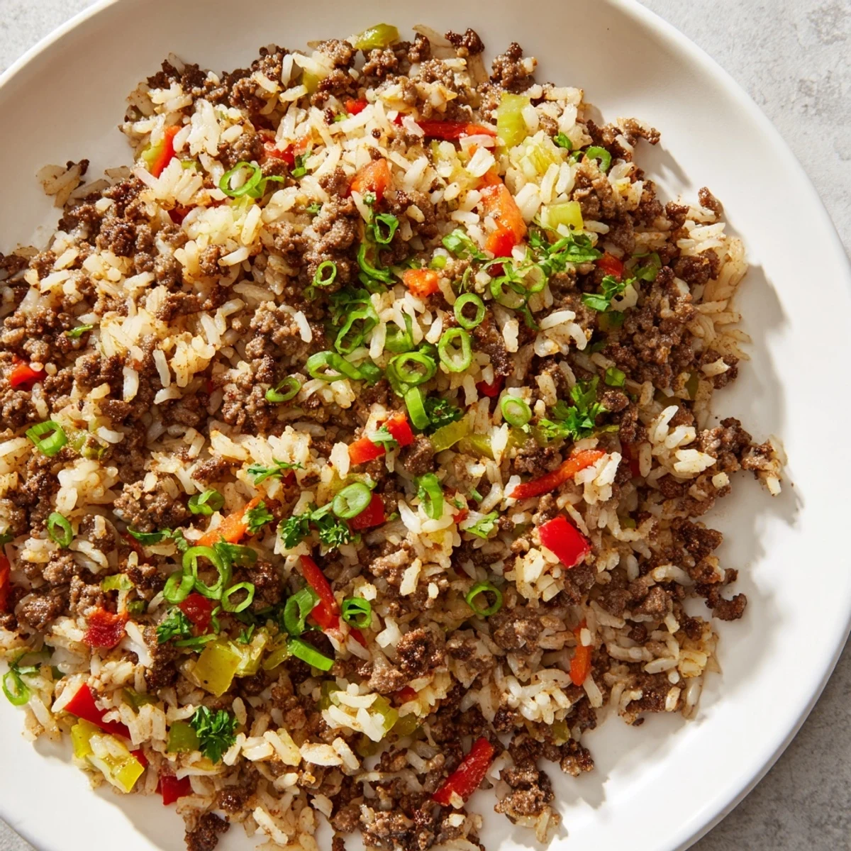Cajun Dirty Rice with Ground Beef and Peppers is served steaming in a skillet, garnished with fresh parsley and sliced green onions.  