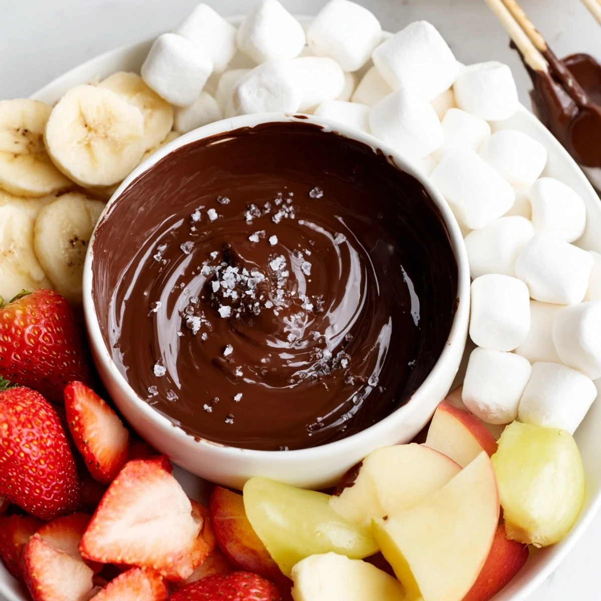 A warm pot of Romantic Chocolate Fondue with marshmallows and fresh strawberries, bananas, and apple slices for dipping.