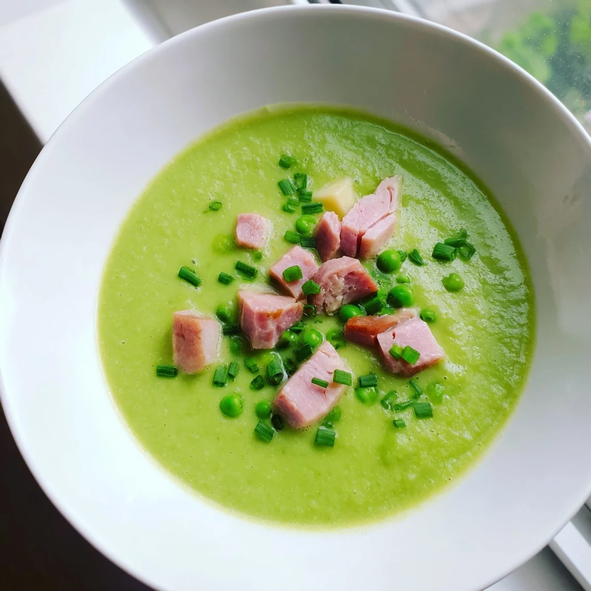 A close-up of Spring Pea Soup with Turkey Ham, featuring fresh thyme garnish and a slice of crusty bread.
