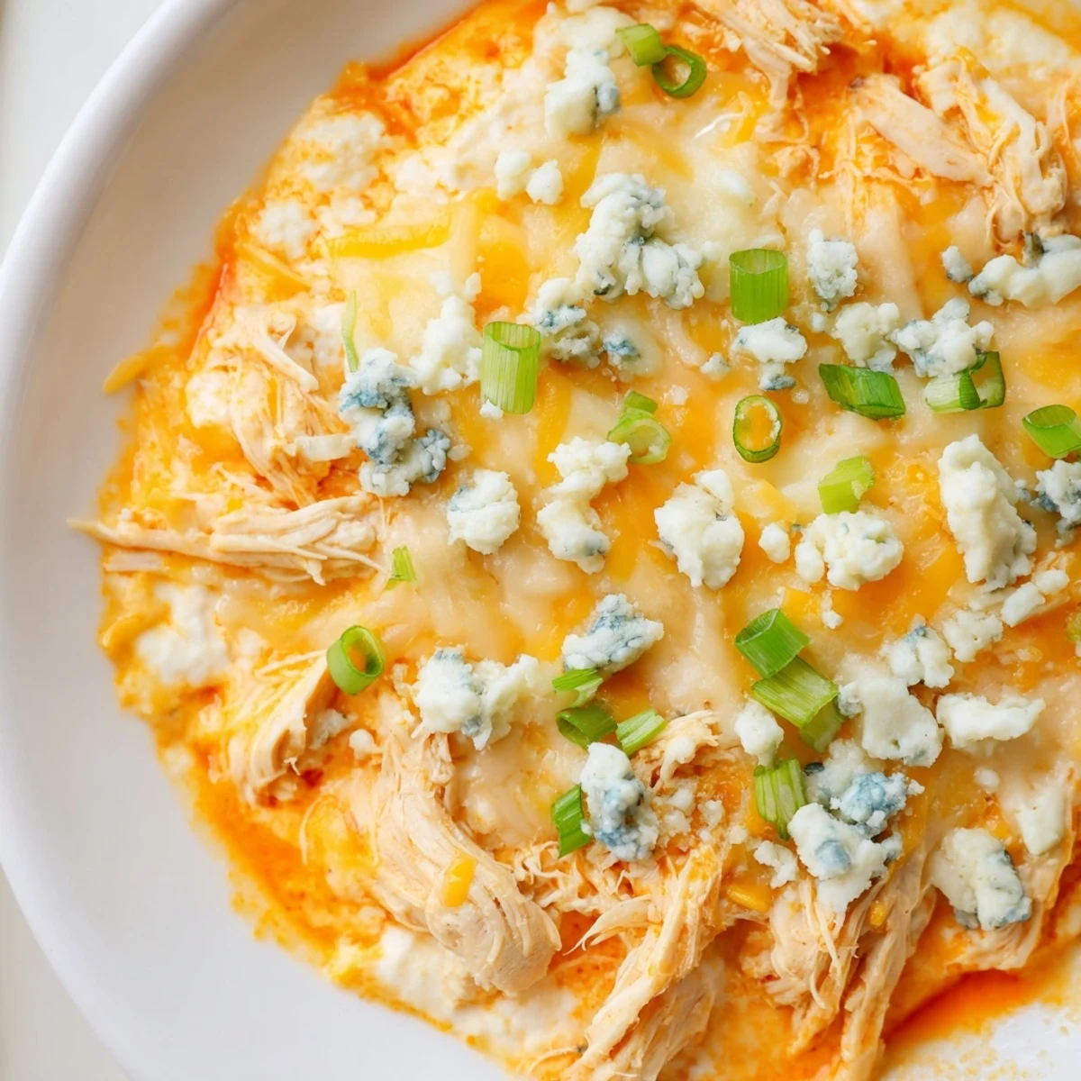 Golden baked Keto Buffalo Chicken Dip with bubbly melted cheese, garnished with green onions and blue cheese crumbles.