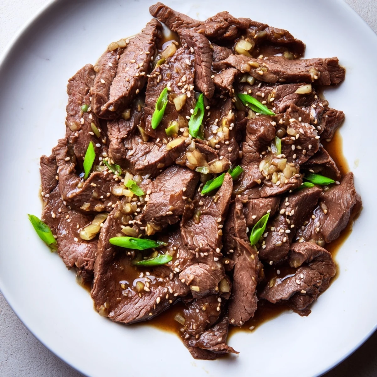 Ultimate Slow Cooker Mongolian Beef sliced thin in a glossy, savory-sweet sauce with garlic and ginger on a dinner plate.