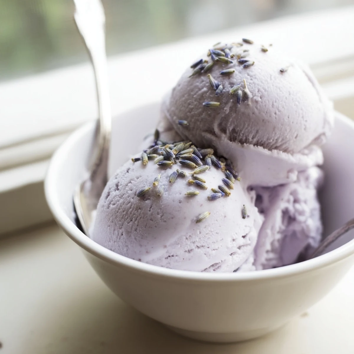 Creamy scoops of Lavender Ice Cream in a chilled bowl, garnished with edible flowers and served with shortbread cookies.