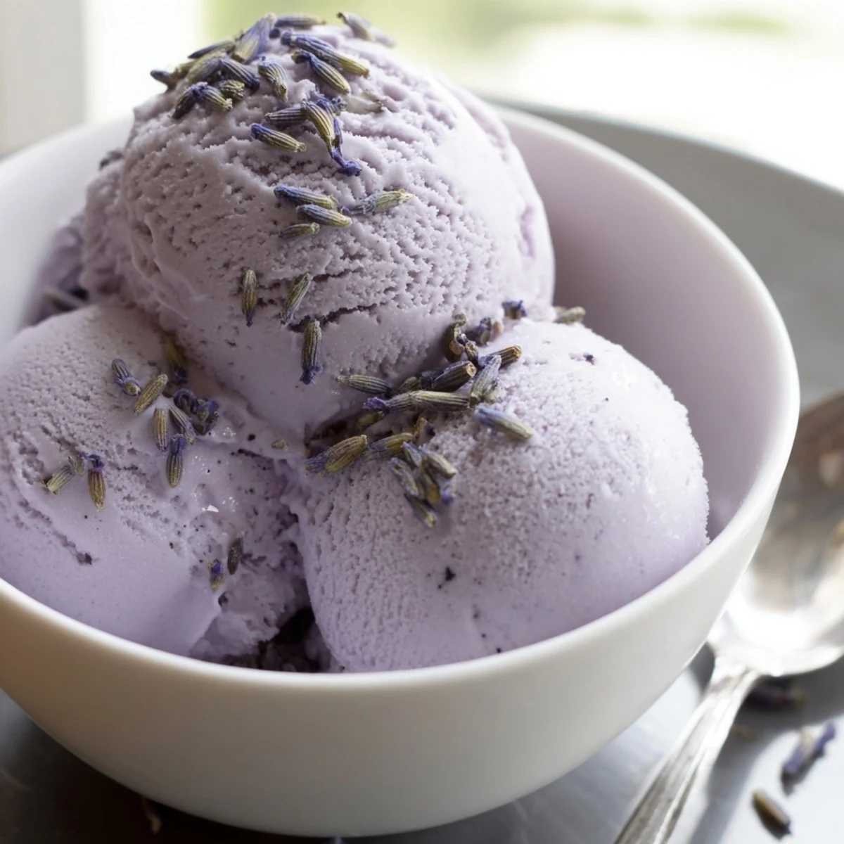 A close-up of homemade Lavender Ice Cream, with a smooth texture and delicate lavender buds sprinkled on top.