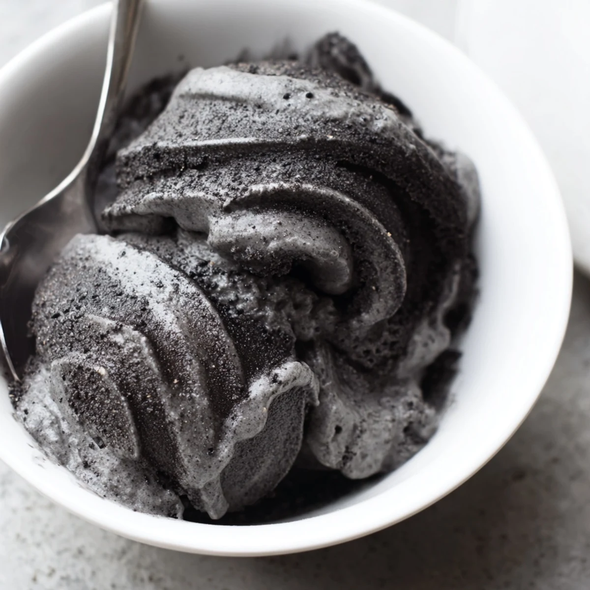 Creamy toasted black sesame ice cream in a ceramic bowl, garnished with seeds and honey.