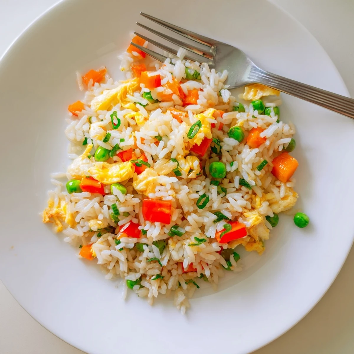 A close-up of golden Fried Rice with scrambled eggs, green onions, and tender vegetables on a plate.  