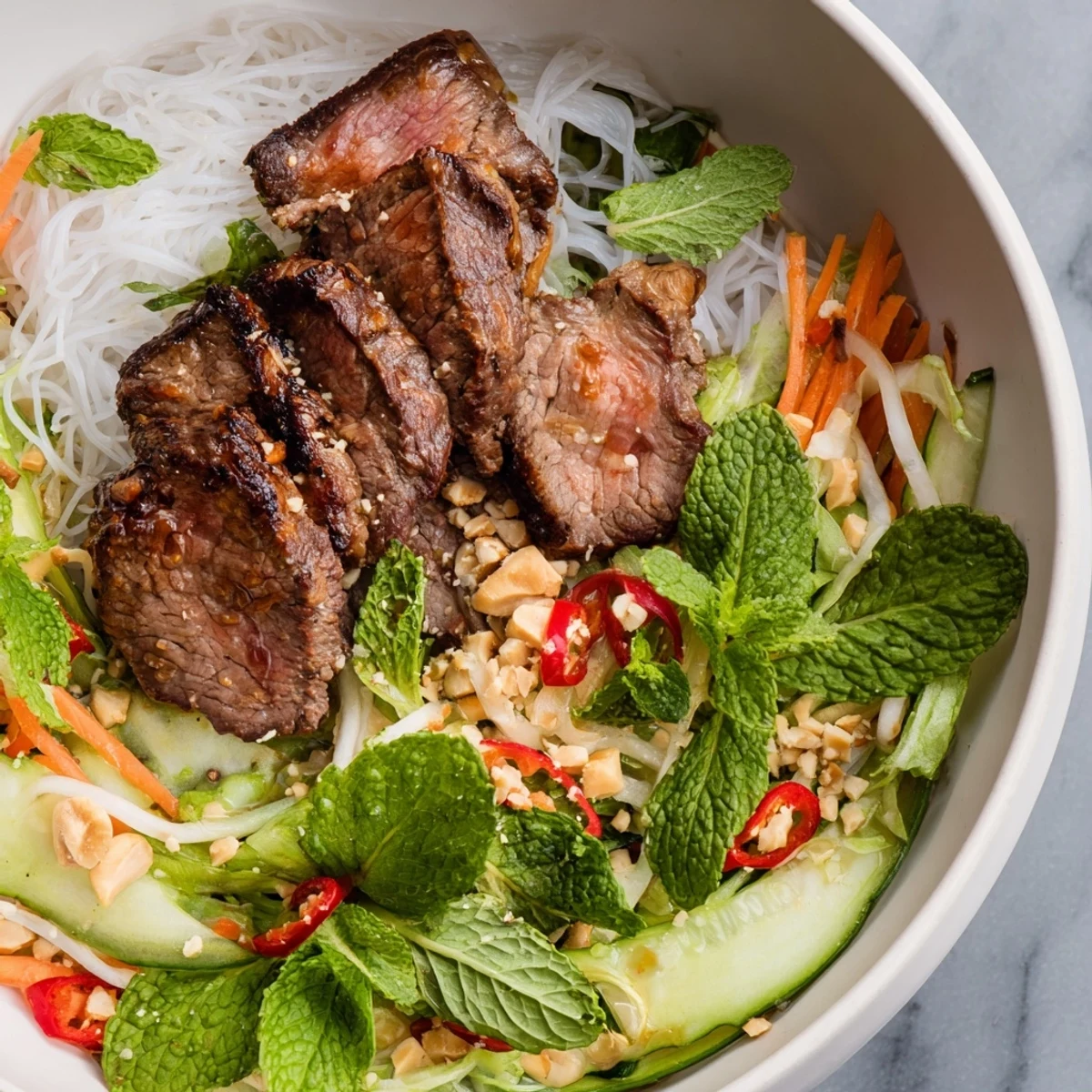 Fresh Bun Bo Xao salad bowl topped with sautéed beef slices and vibrant herbs, drizzled with tangy nuoc cham dressing.