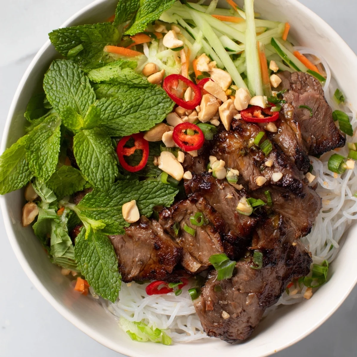 Close-up of Bun Bo Xao with rice vermicelli, crisp vegetables, and chopped peanuts, served as a colorful Vietnamese main dish.