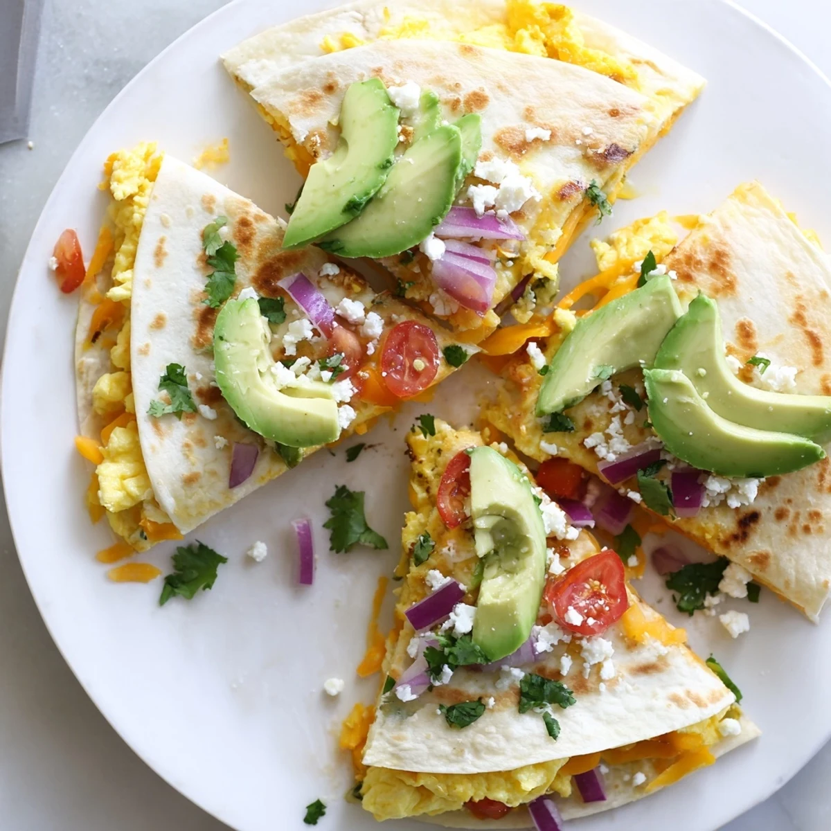A close-up of Spicy Avocado Egg and Three Cheese Quesadillas shows creamy avocado slices and fluffy scrambled eggs tucked inside crispy flour tortillas.