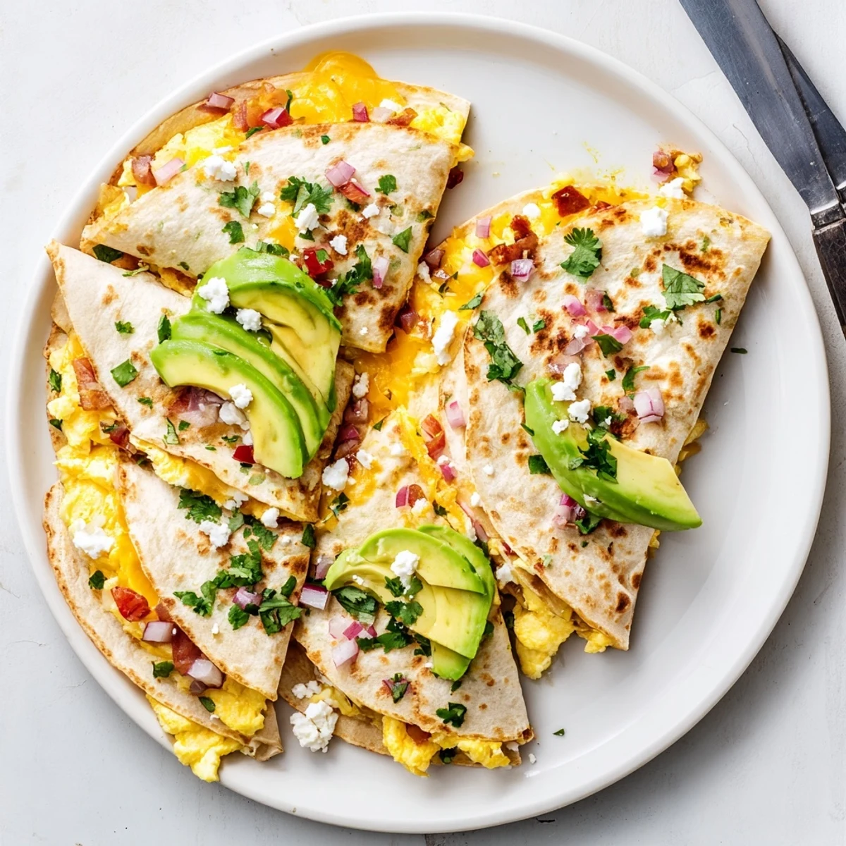 Overhead view of Spicy Avocado Egg and Three Cheese Quesadillas served with sour cream, salsa, and lime wedges on a rustic table.