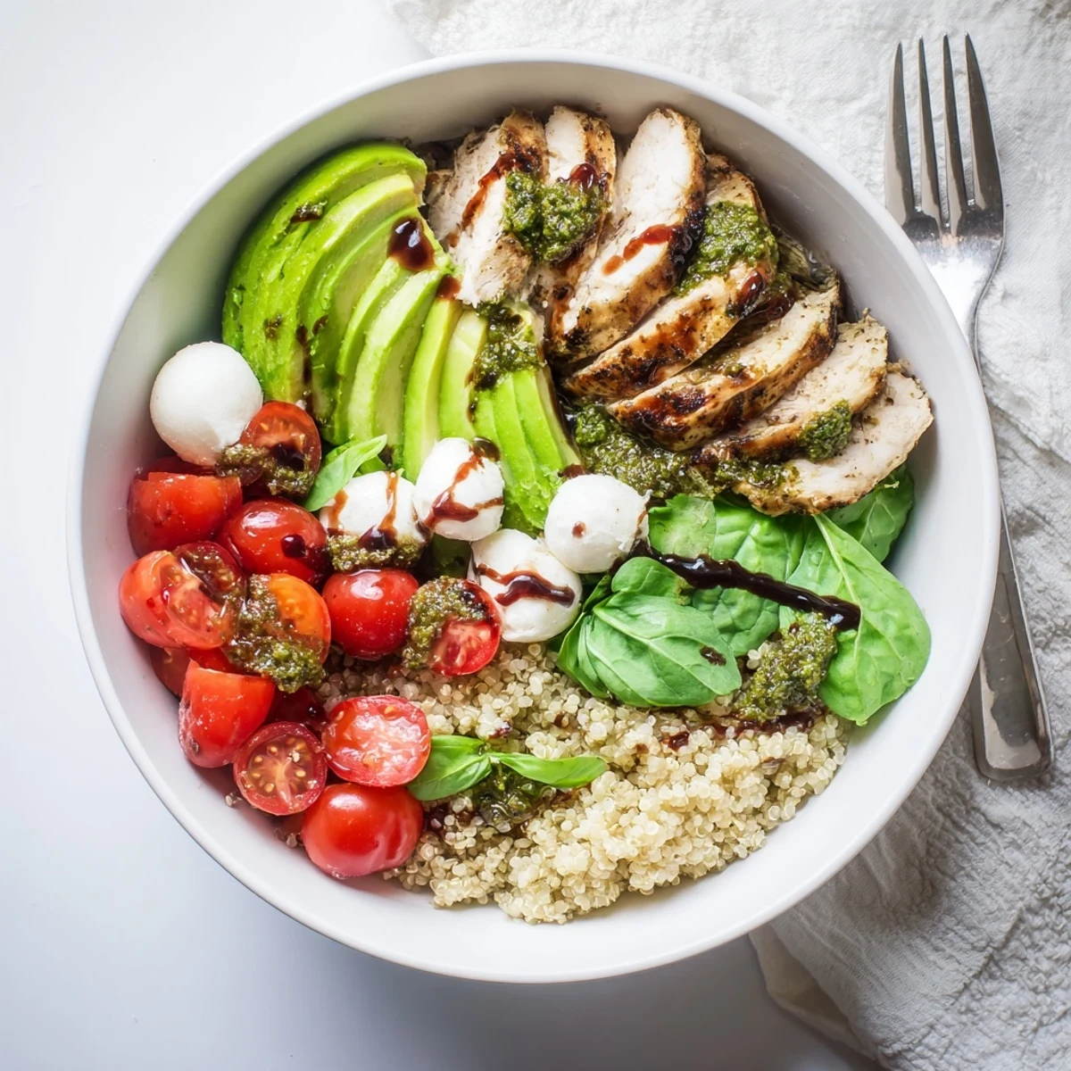 Hearty Pesto Chicken Caprese Grain Bowl drizzled with balsamic and served over greens.