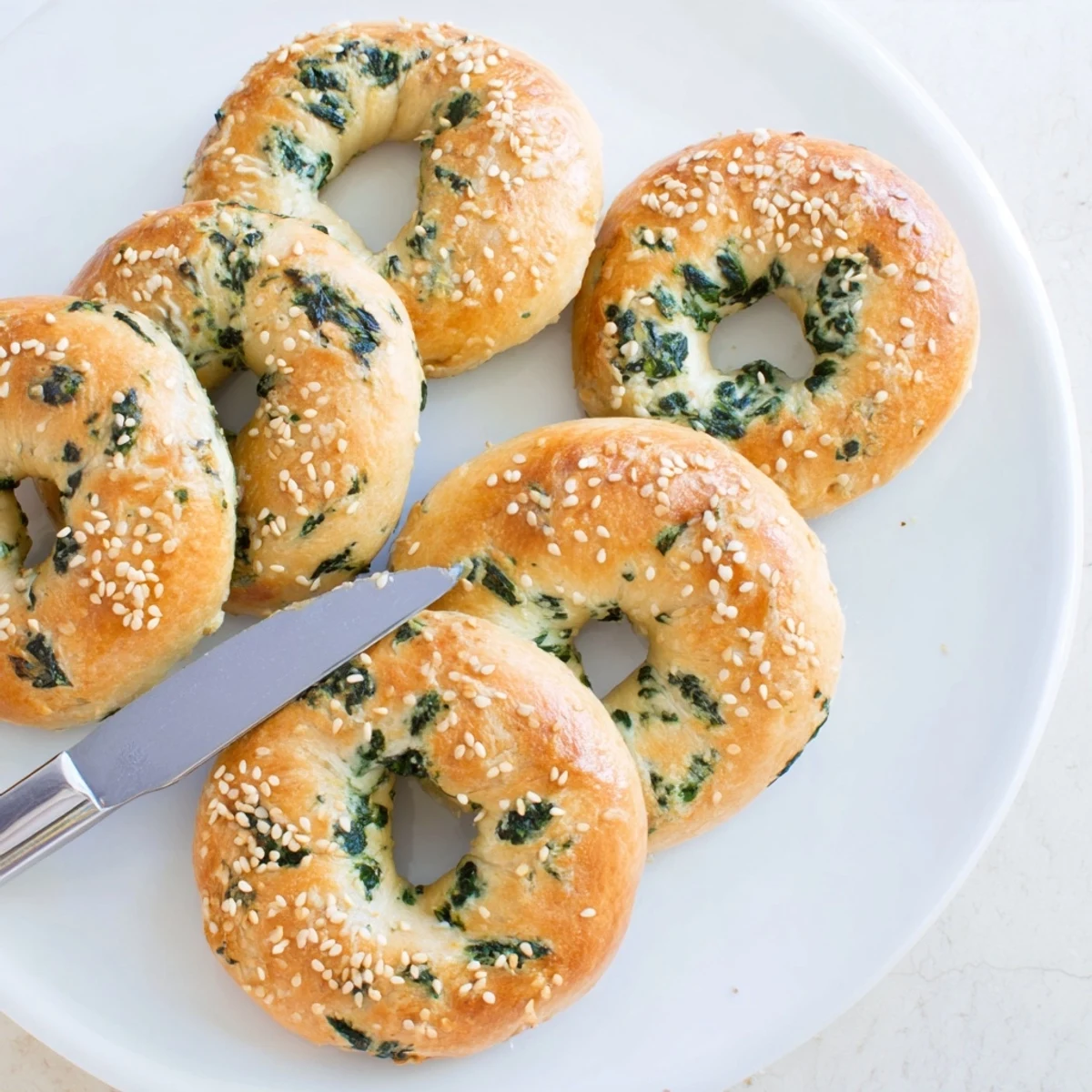 Stack of warm Spinach Cottage Cheese Flagels served on a wooden board with butter and a spread of cream cheese.