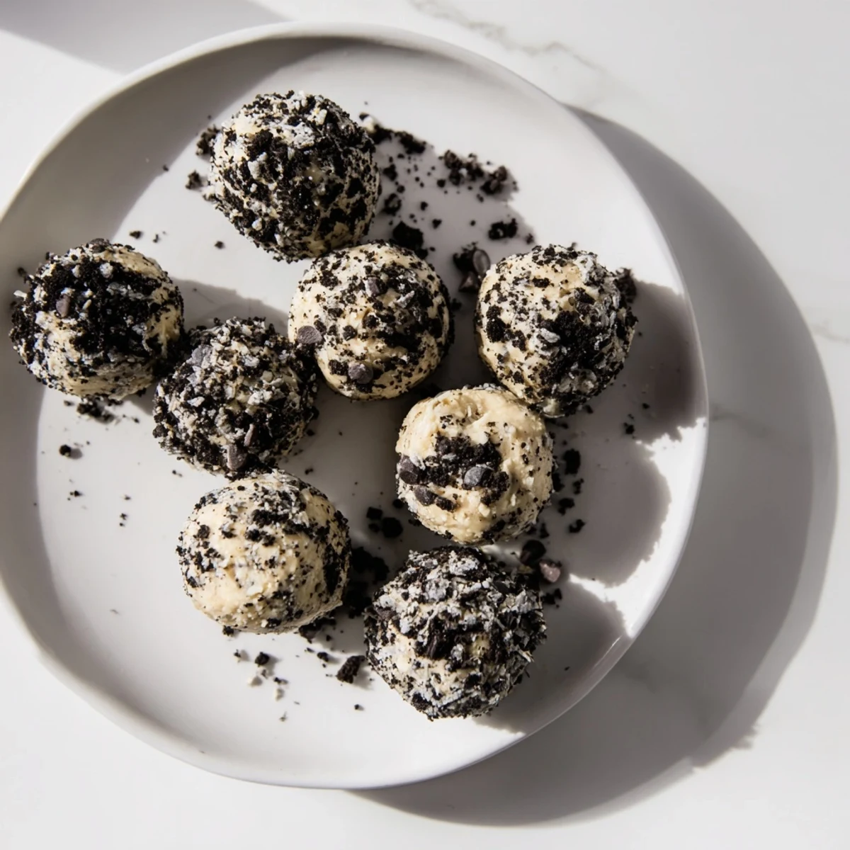 A hand holding a bite-sized Cream Cheese Oreo Protein Ball, revealing a creamy texture and Oreo specks inside.