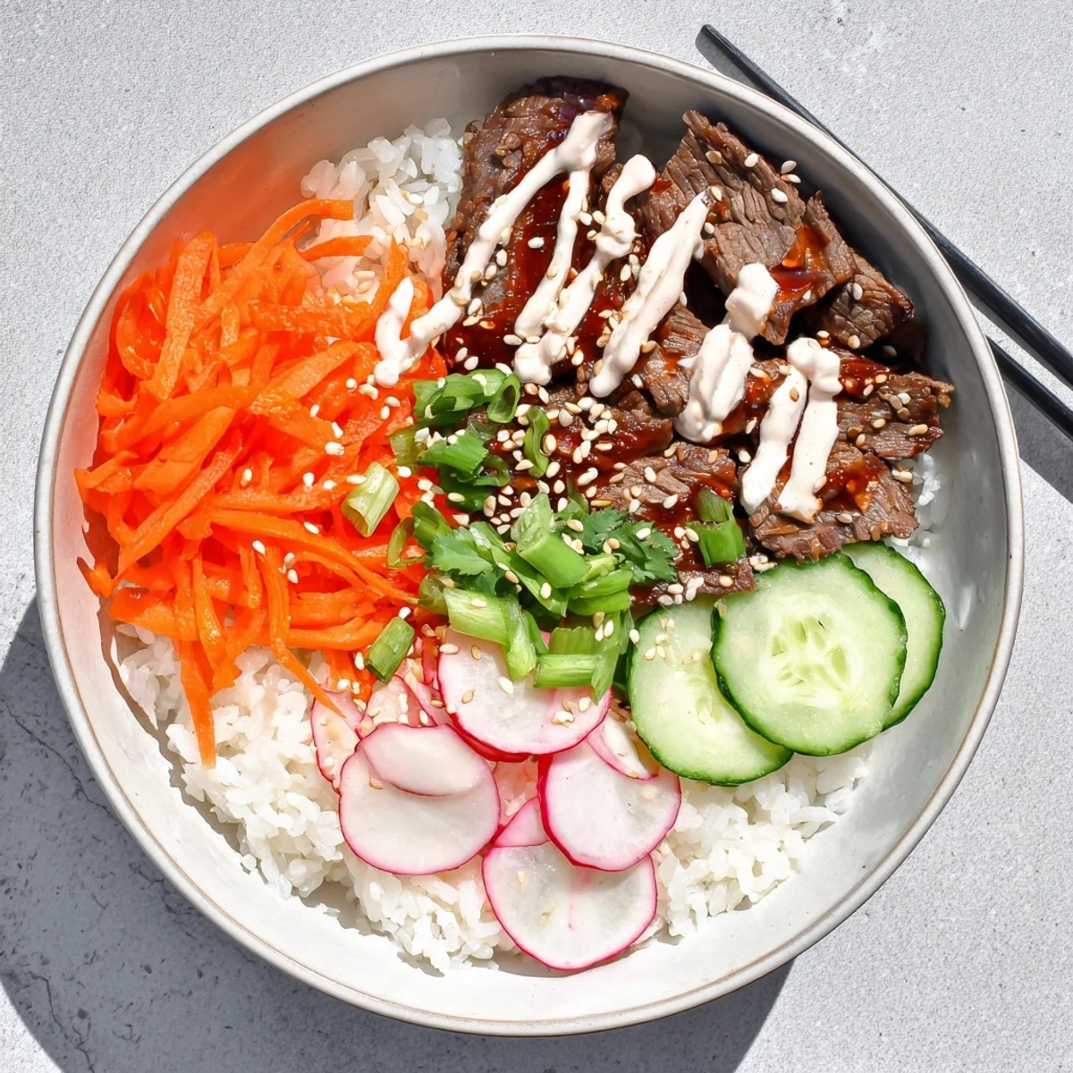 A close-up of Korean BBQ Steak Rice Bowls with Spicy Cream Sauce shows juicy steak slices, fresh carrots and cucumbers, and a rich sauce pooling on white rice.