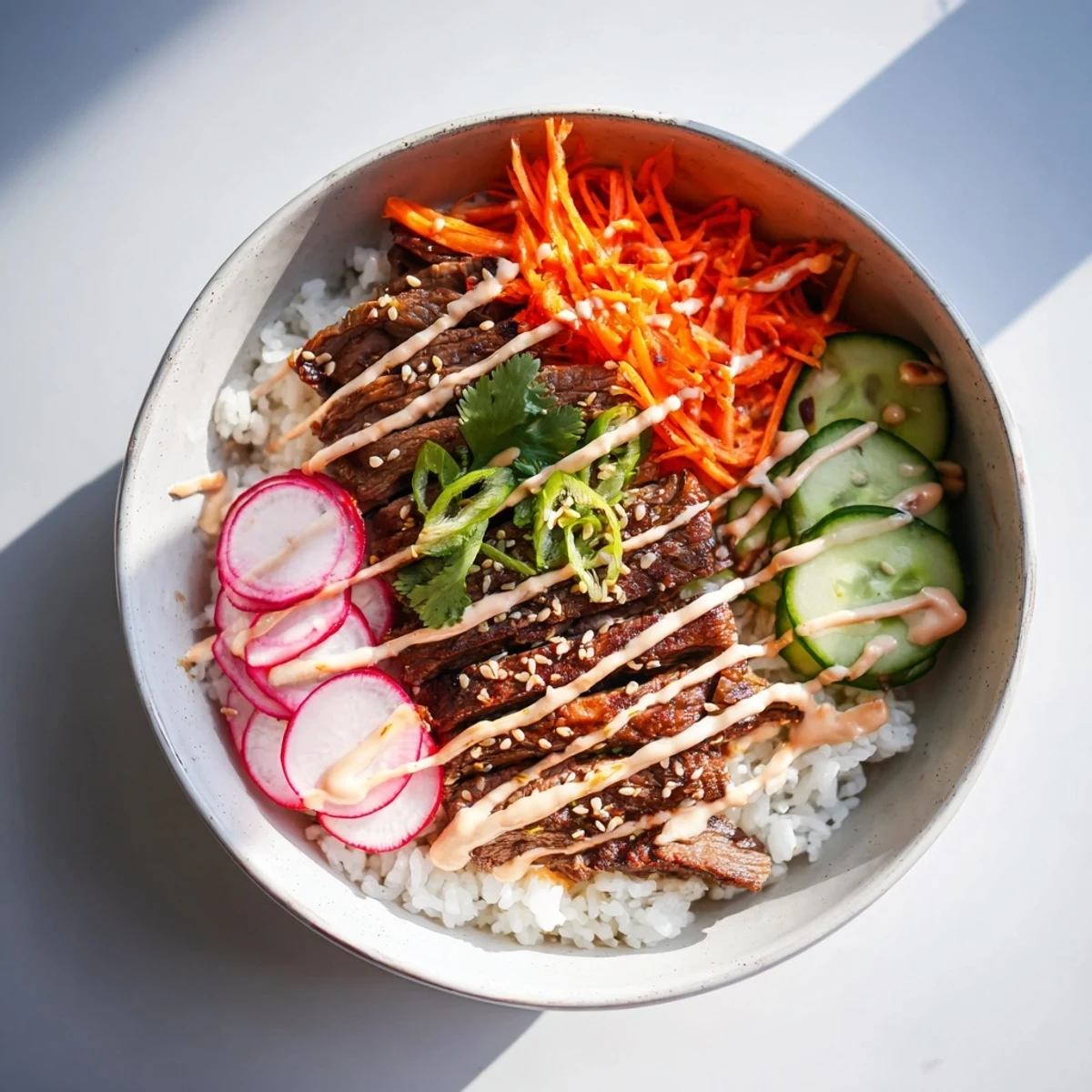 Overhead view of Korean BBQ Steak Rice Bowls with Spicy Cream Sauce highlights steamed rice, colorful toppings, and a generous swirl of spicy cream sauce ready to eat.