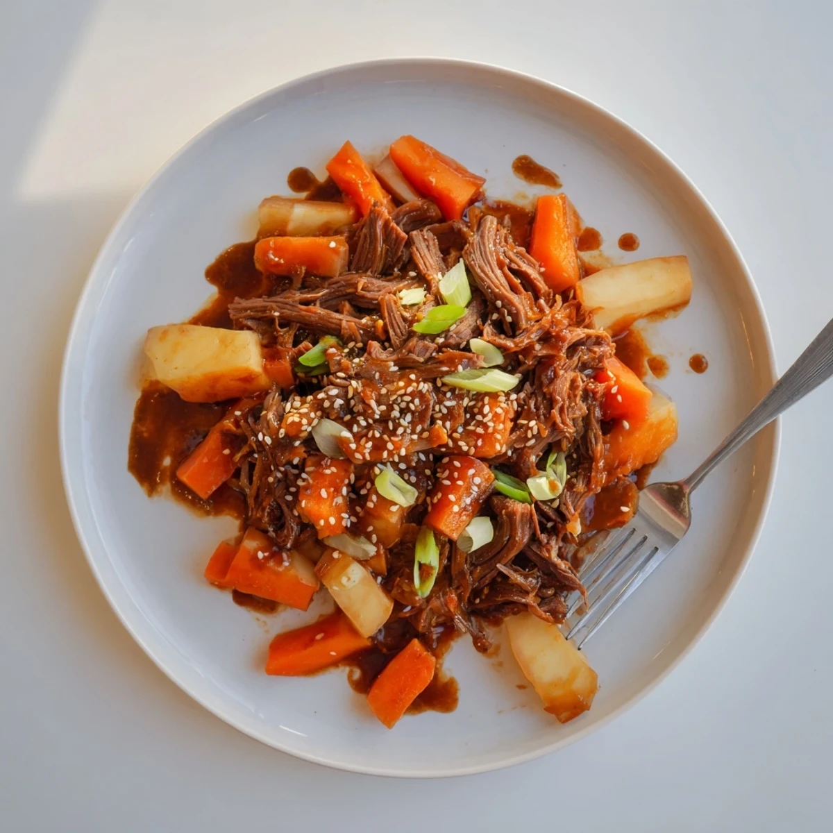 Slow-cooked Korean Style Pot Roast falling apart on a platter, surrounded by soft vegetables and drizzled with a rich, glossy sauce.
