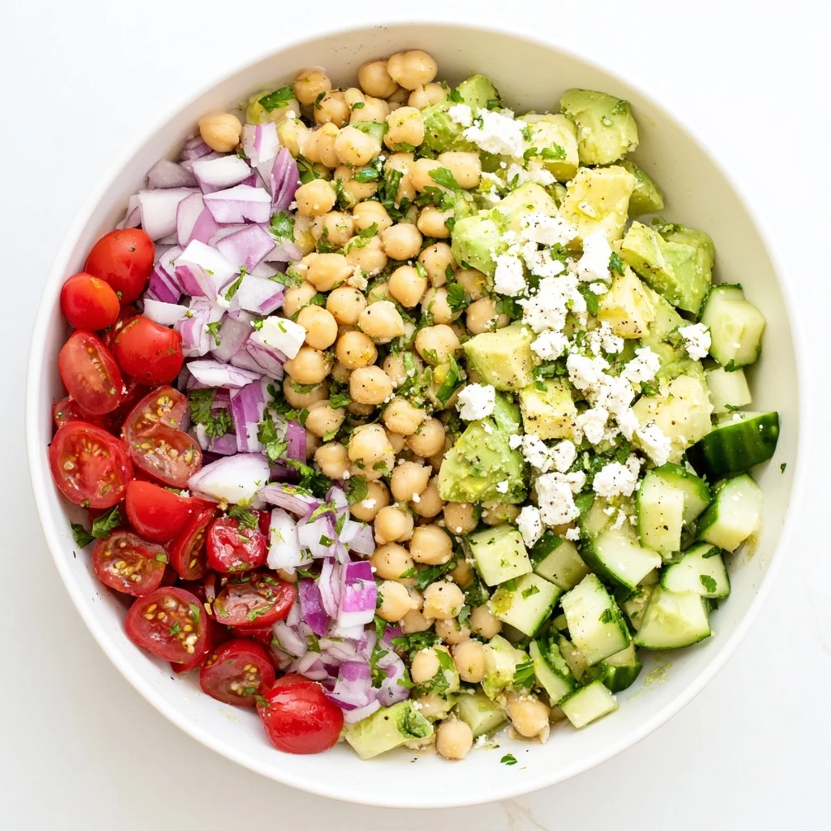 Chickpea Feta Avocado Salad in a white ceramic bowl, garnished with parsley and served beside pita bread slices.