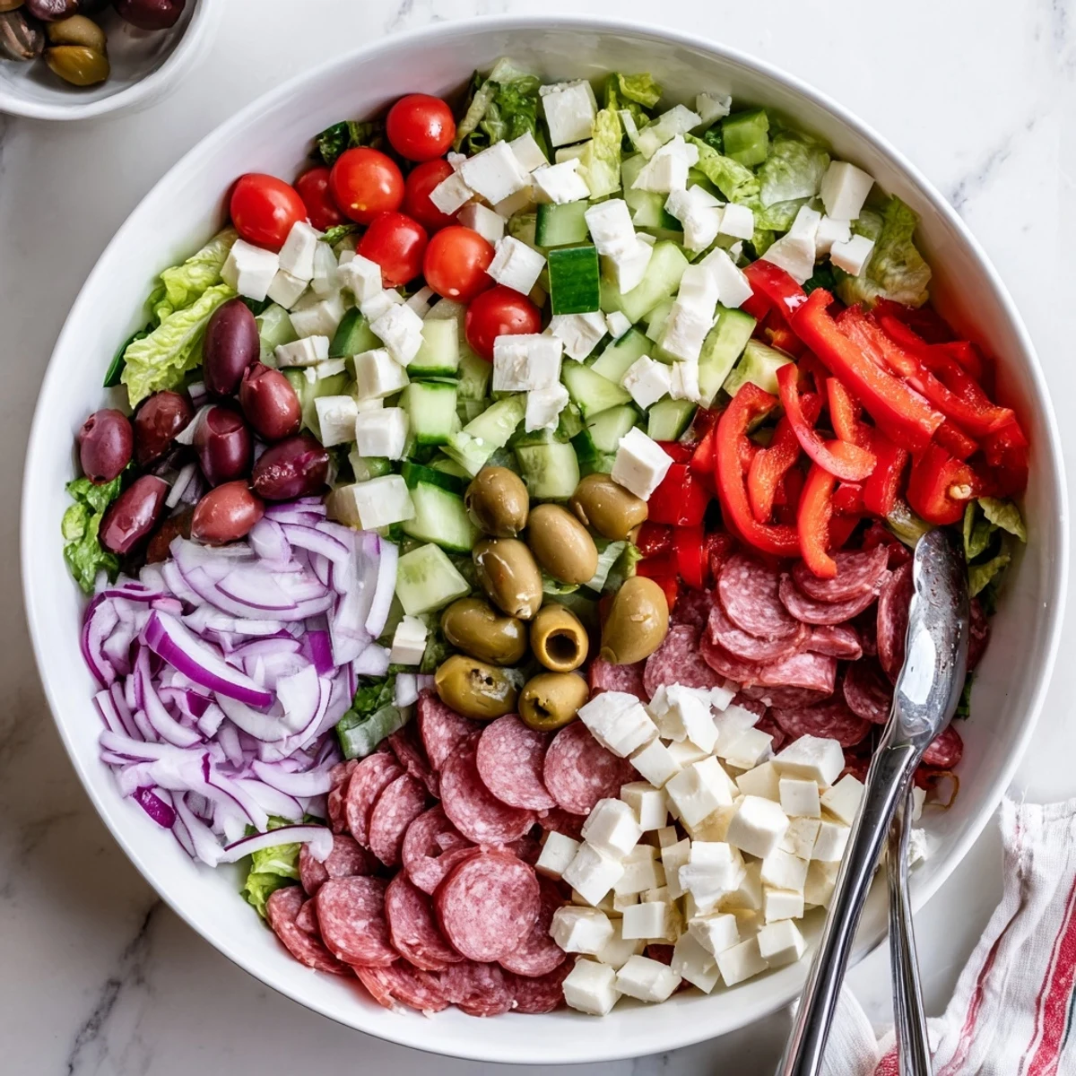 Homemade Italian chopped salad overflowing with crunchy vegetables, salami cubes, and Kalamata olives coated in olive oil dressing
