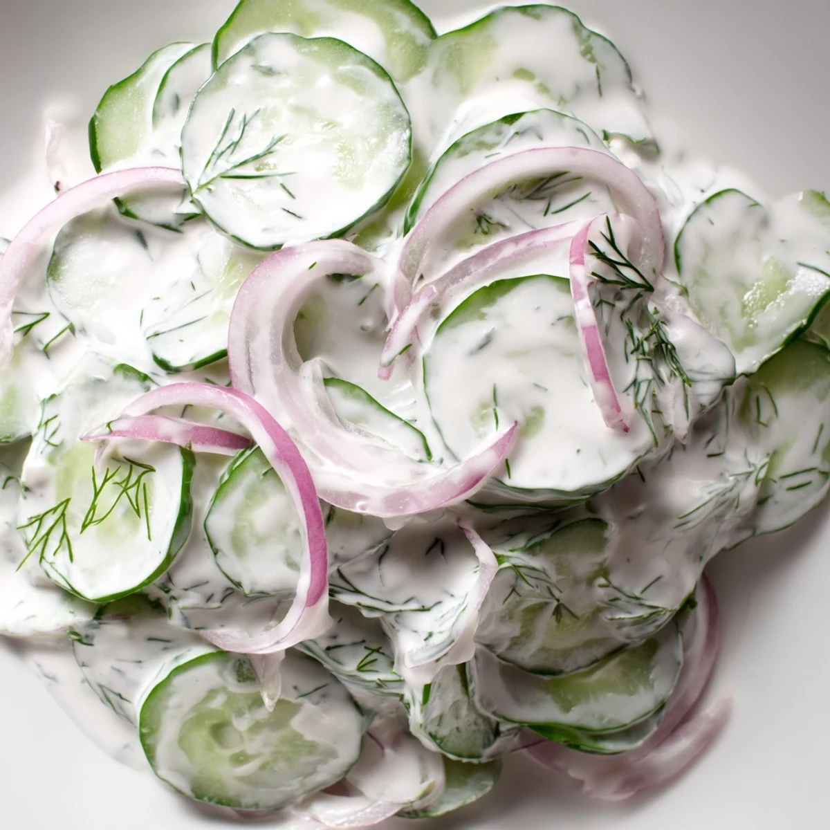 Creamy cucumber salad featuring crisp sliced cucumbers and red onions in a tangy white dressing with fresh dill garnish