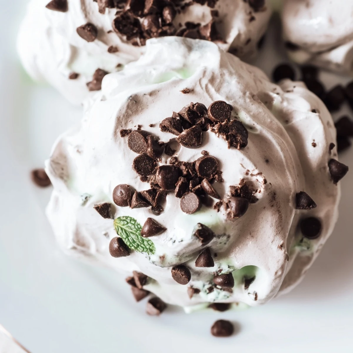 Dreamy dark chocolate and mint chip clouds meringue cookies piled on a white baking sheet