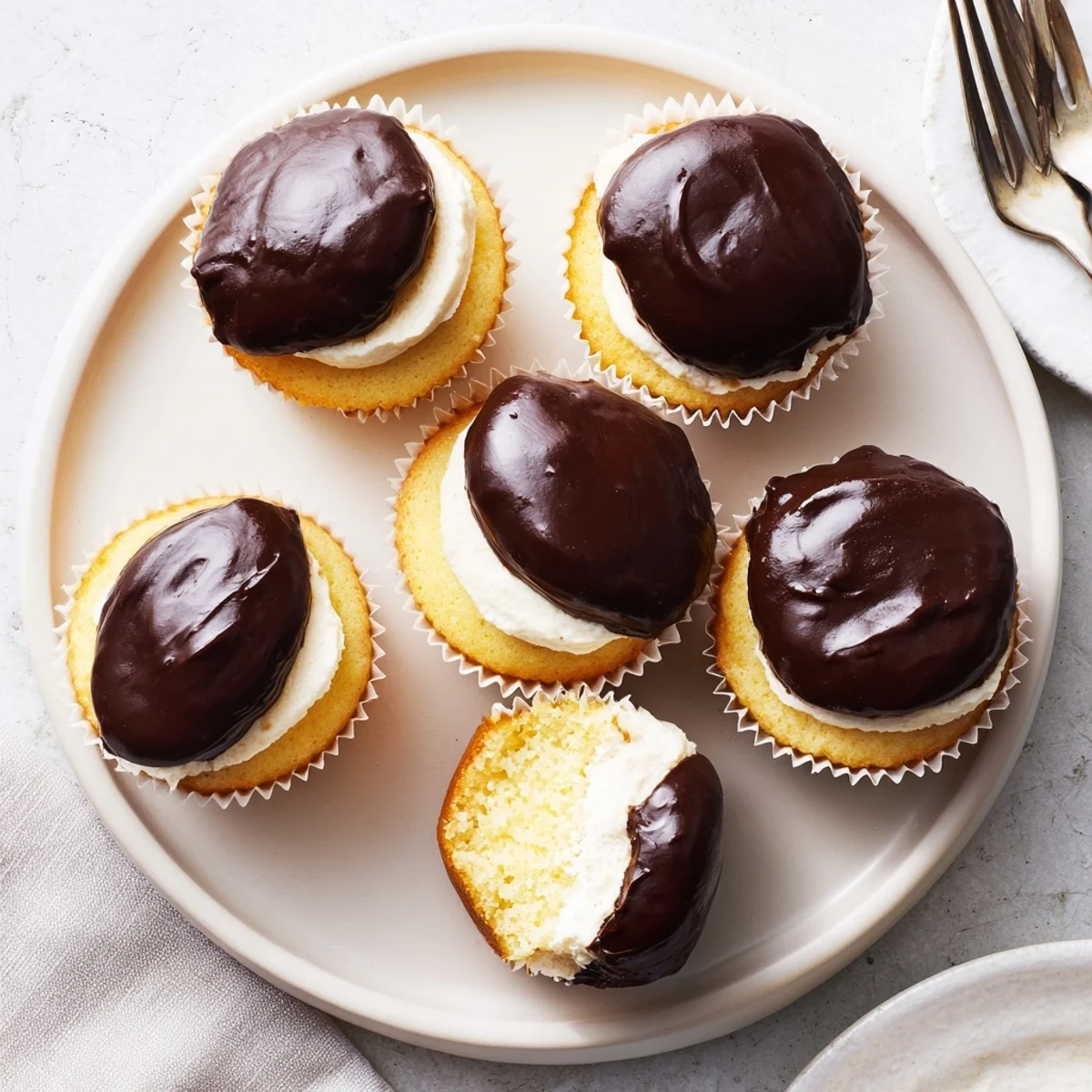 Golden vanilla Boston cream pie cupcakes topped with glossy chocolate ganache and filled with creamy custard