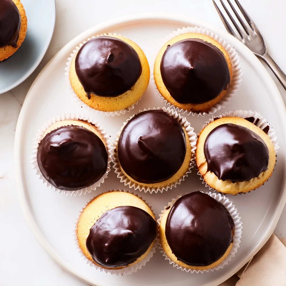 Individual Boston cream pie cupcakes with silky pastry cream centers and decadent poured chocolate topping