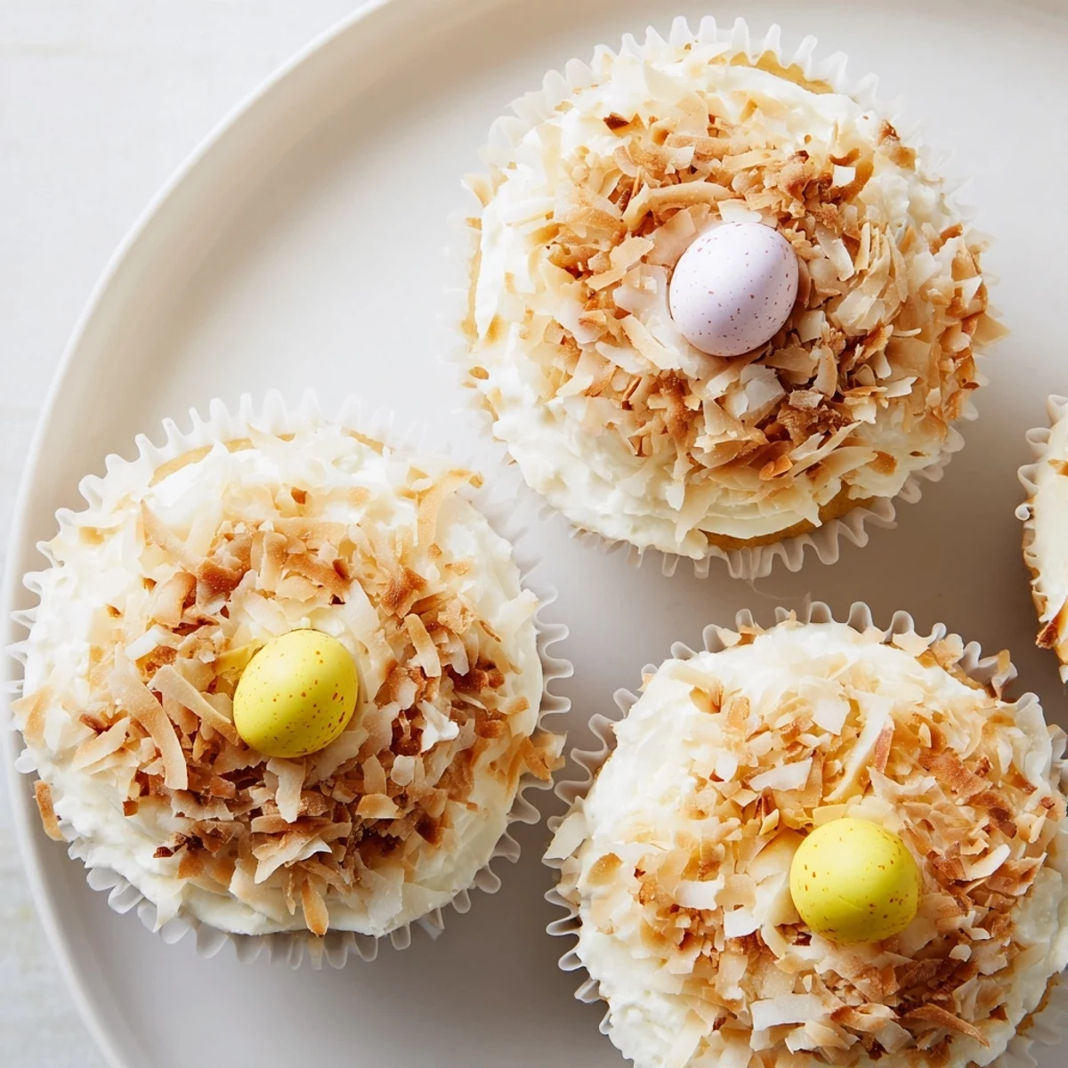 Easter-themed vanilla cupcakes with coconut buttercream nests holding pastel mini chocolate eggs on top
