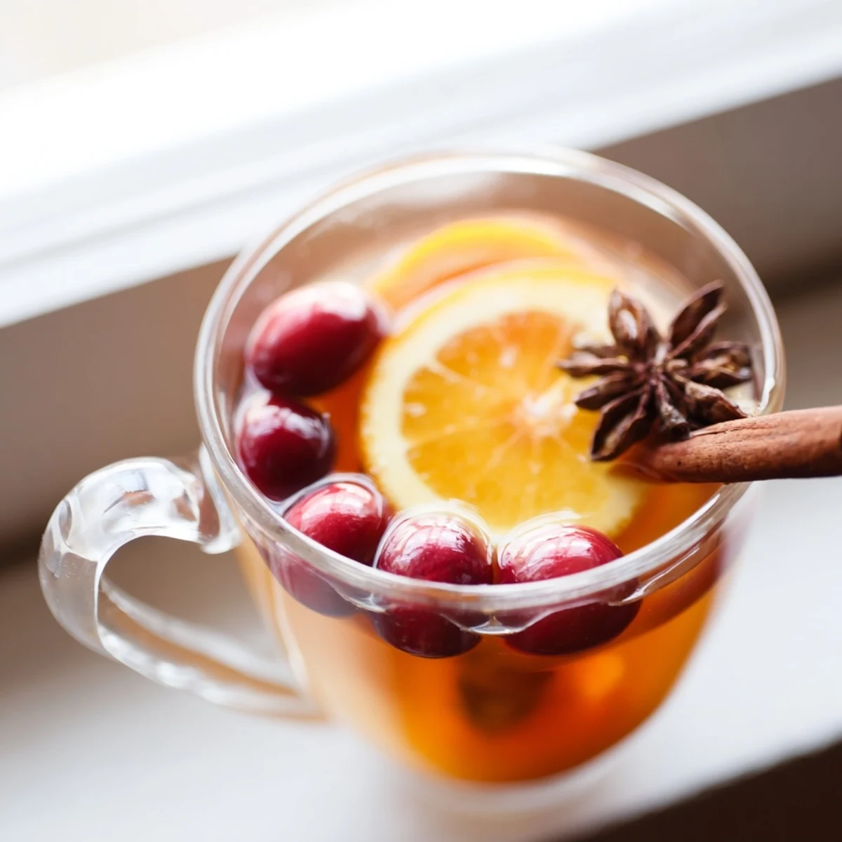 Rustic mug of spiced Orange Cranberry Tea with cinnamon stick and star anise on wooden table