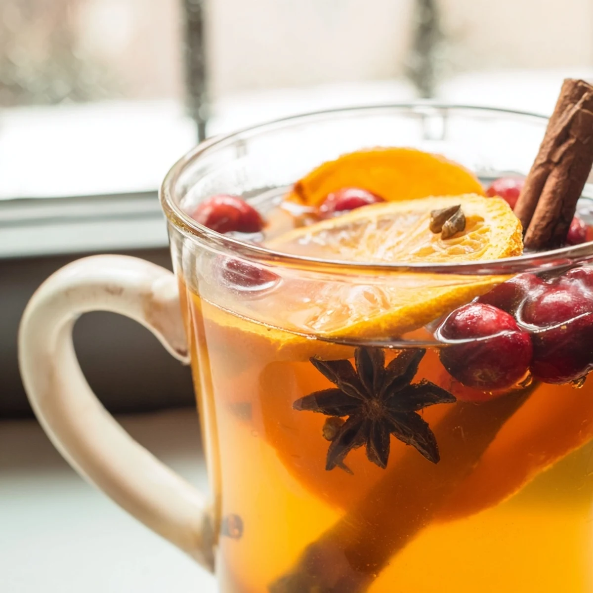 Glass pitcher of vibrant red Orange Cranberry Tea poured over ice with orange wheel garnish