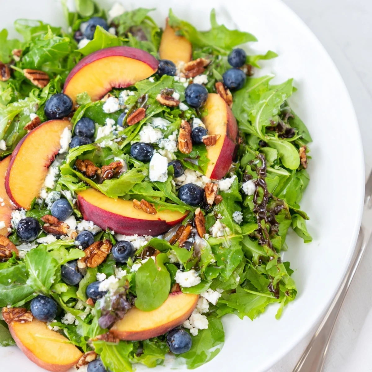 Vibrant summer salad bowl piled high with juicy peaches blueberries and crumbled feta cheese over greens