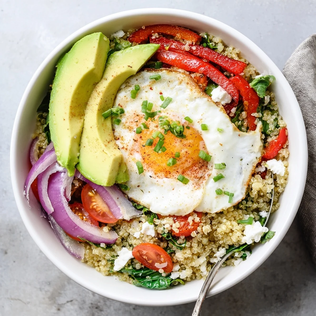 Savory quinoa breakfast bowl topped with fried egg, colorful vegetables, and fresh herbs