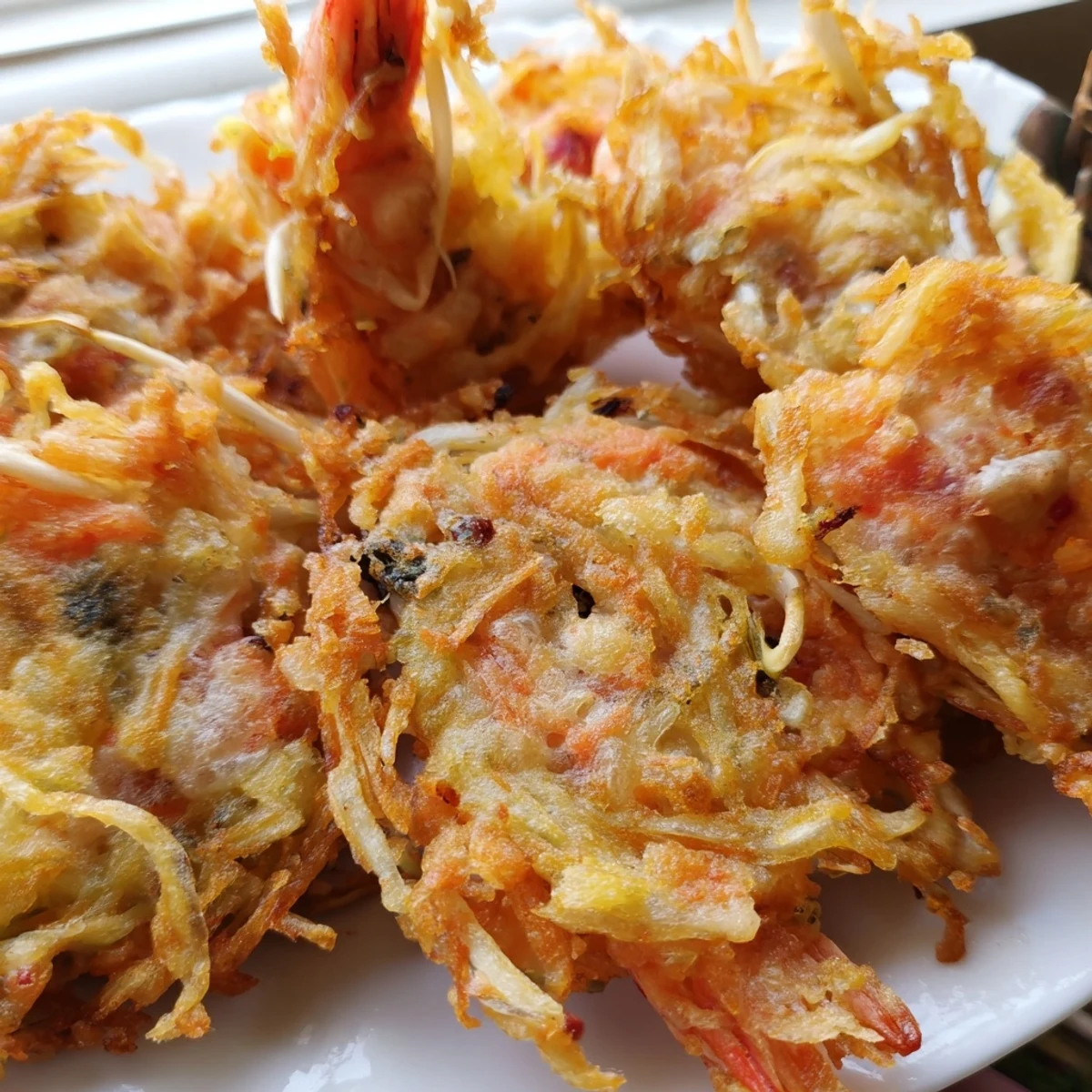 Golden crispy Ukoy Filipino shrimp fritters topped with visible vegetables on a white plate