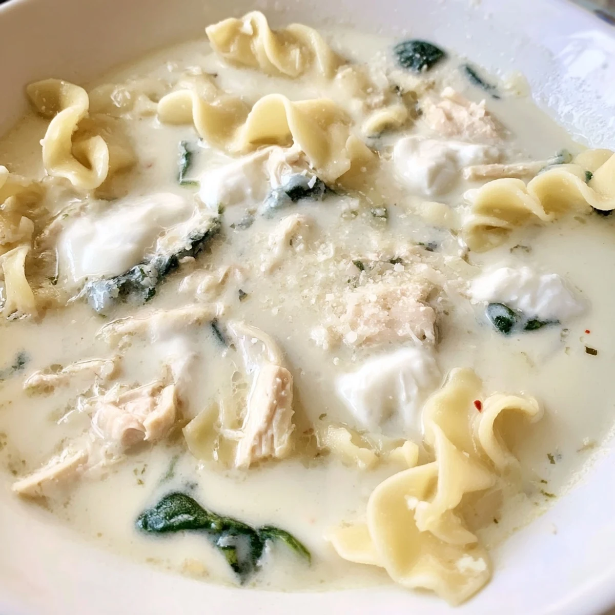 Thick cheesy white lasagna soup loaded with shredded chicken and wilted spinach in a rustic pot