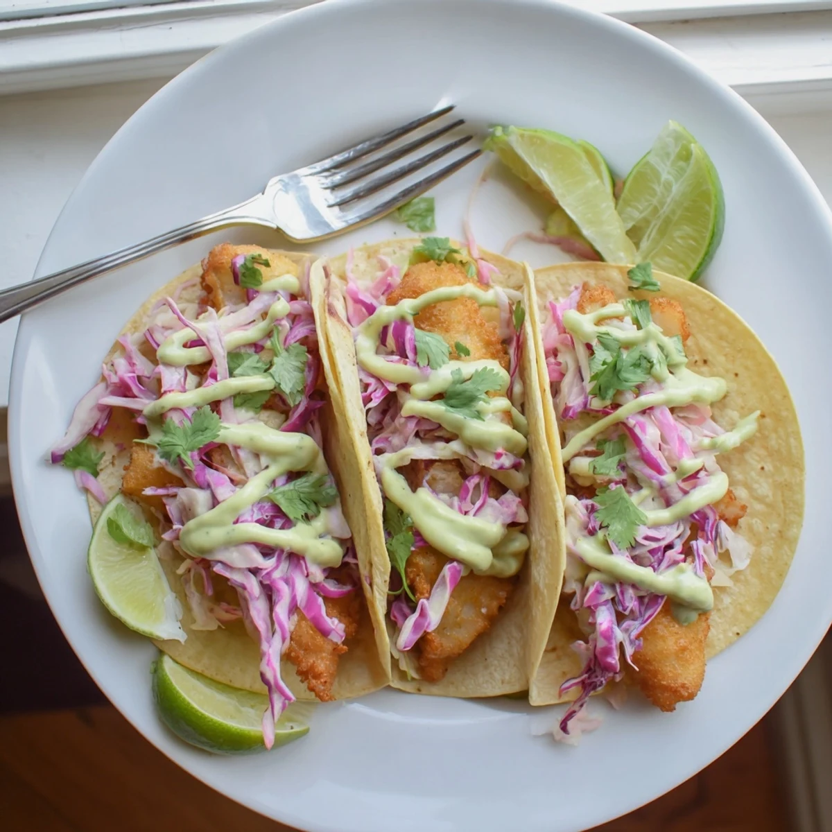 Crispy golden Baja fish tacos topped with vibrant cabbage slaw and creamy avocado crema drizzle