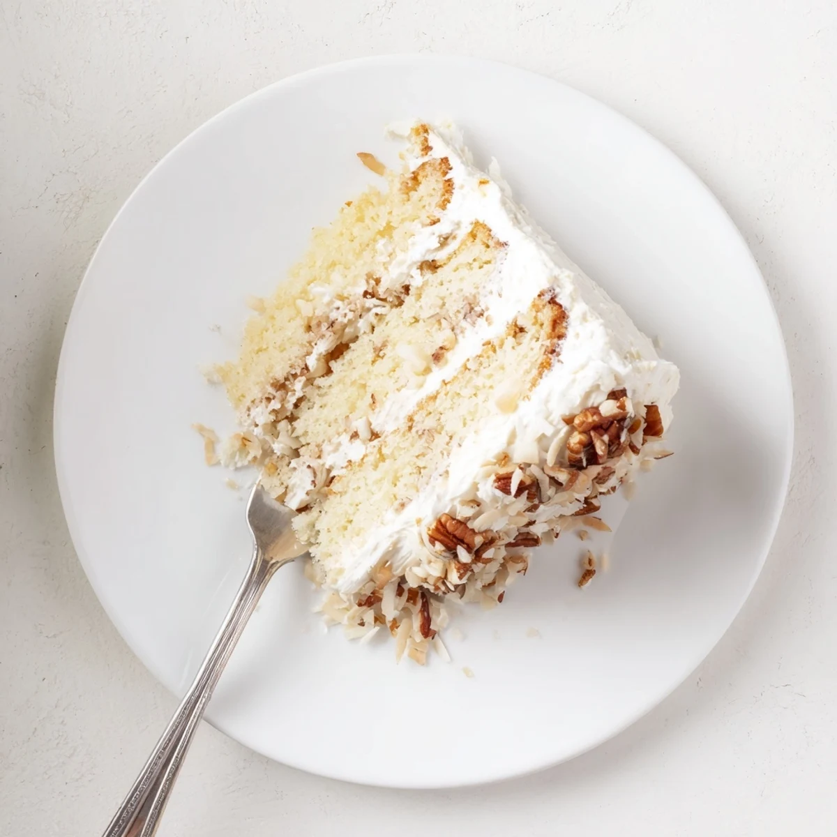 Slice of Quick Italian Cream Cake showing tender crumb studded with toasted coconut and chopped pecans beneath smooth frosting
