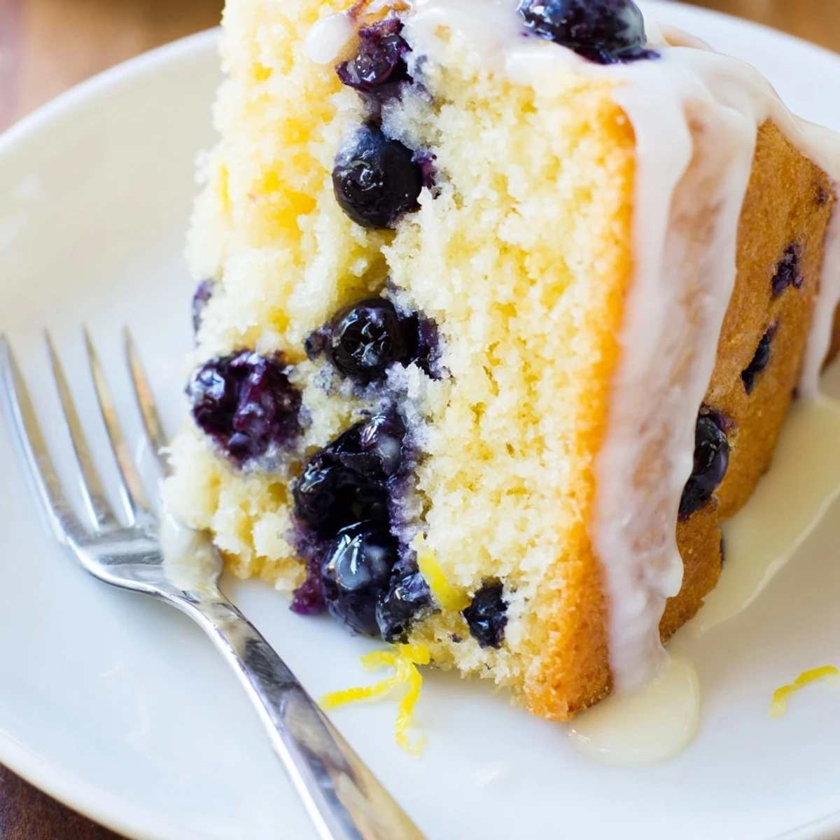 Golden slice of moist lemon blueberry cake topped with sweet white glaze and fresh blueberries