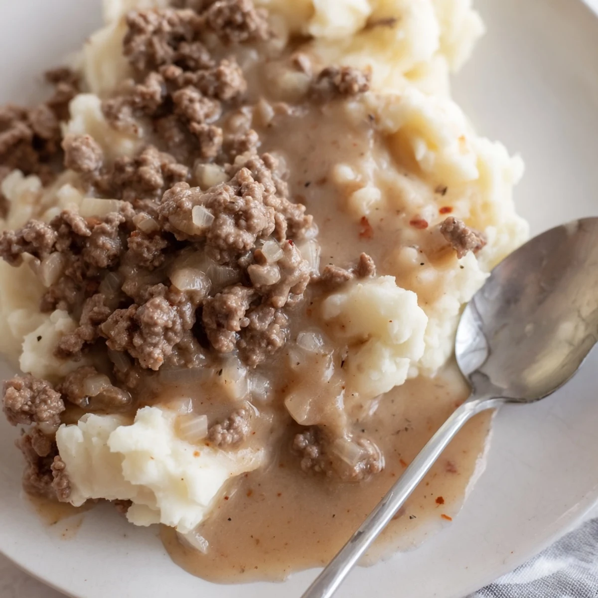 Creamy homemade hamburger gravy ladled generously over fluffy mashed potatoes in a white bowl