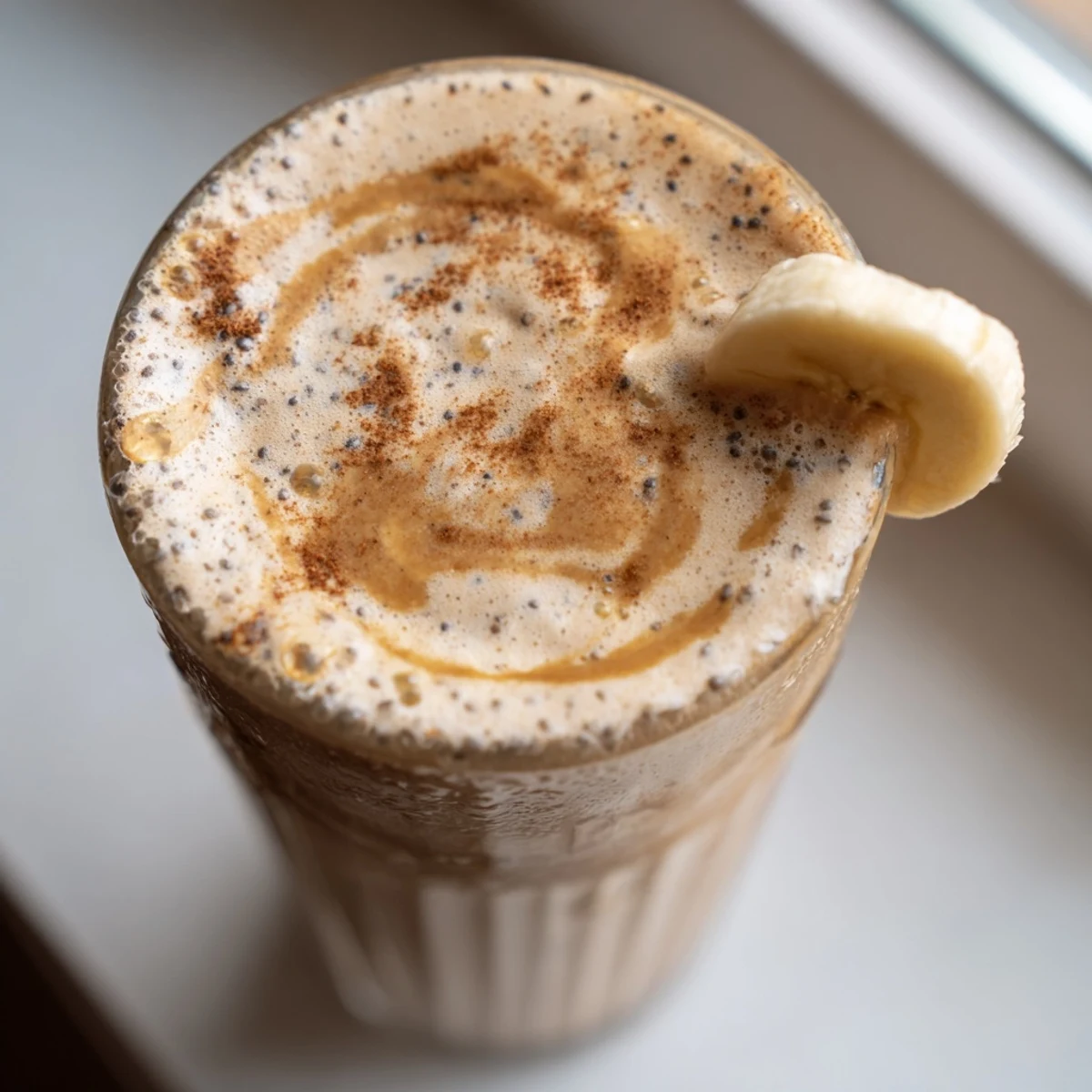 Creamy banana protein coffee smoothie poured into a tall glass topped with cinnamon