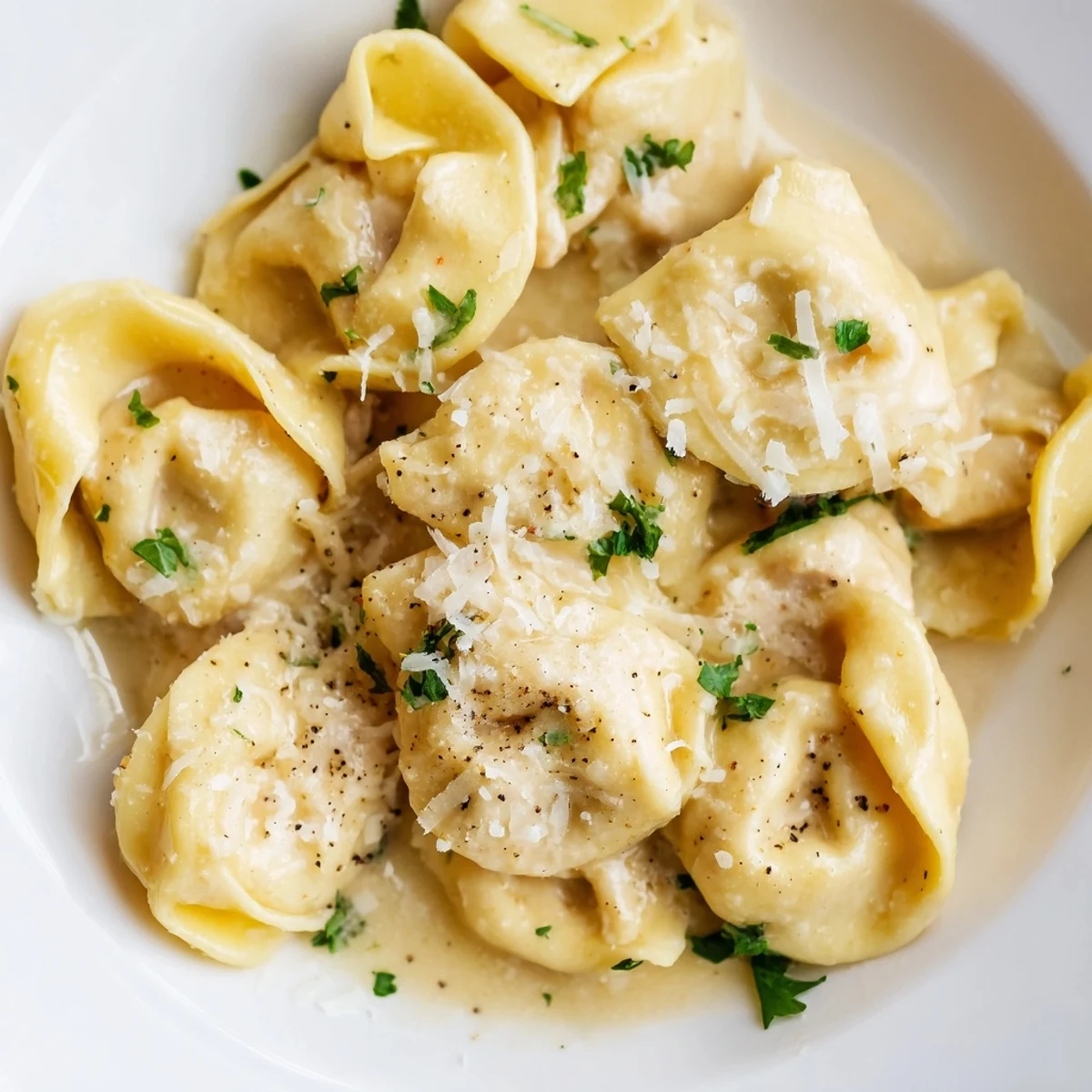 Creamy chicken tortellini plated in a white bowl with fresh parsley garnish