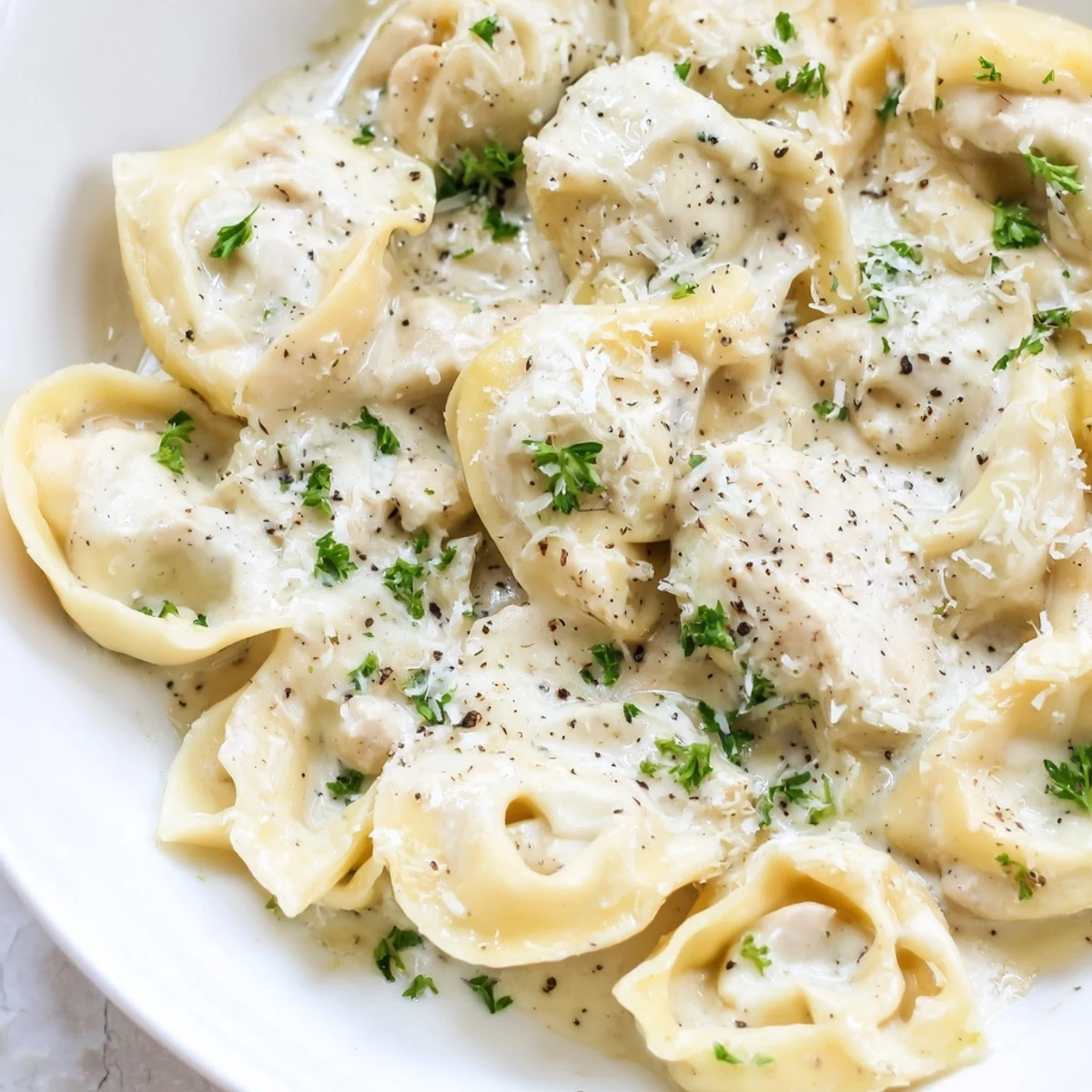 Golden homemade chicken tortellini drizzled with rich Parmesan cream sauce on a rustic plate