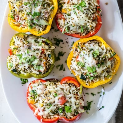 Bright bell peppers stuffed with rice, vegetables, and cheese, garnished with fresh parsley on a rustic plate.